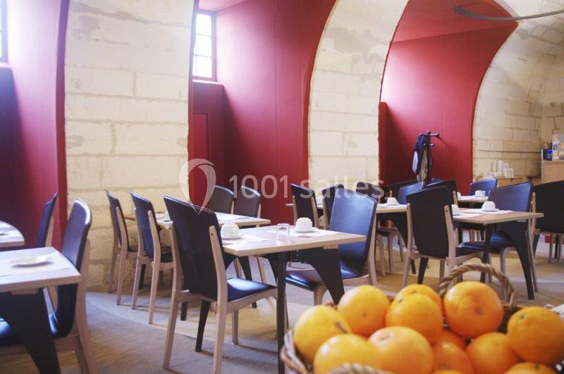 Salle de restaurant lumineuse avec murs en pierre, tables dressées et corbeille d'oranges au premier plan.