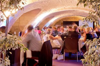 Salle voûtée avec murs en pierre, tables et chaises modernes, buffet en arrière-plan et éclairage chaleureux.