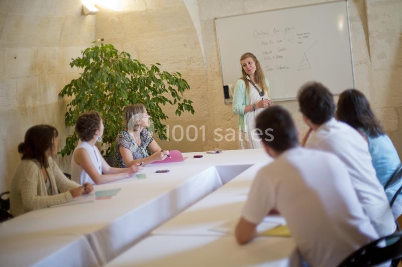 Une femme présente un schéma sur un tableau blanc à un groupe de personnes assises autour d'une table.