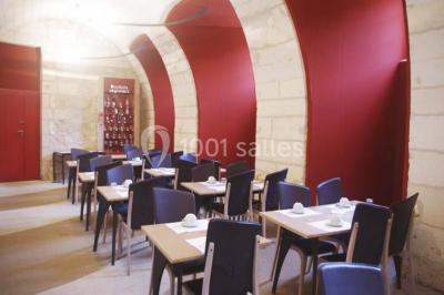 Salle voûtée avec murs en pierre, tables et chaises modernes, buffet en arrière-plan et éclairage chaleureux.