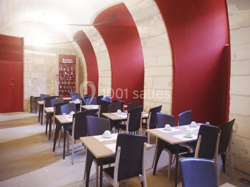 Salle de restaurant avec murs en pierre, tables dressées et chaises bleues, éclairée par une lumière naturelle.