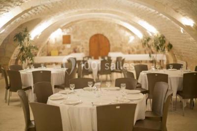 Salle voûtée avec murs en pierre, tables et chaises modernes, buffet en arrière-plan et éclairage chaleureux.