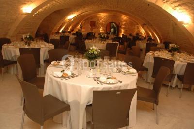 Salle voûtée avec murs en pierre, tables et chaises modernes, buffet en arrière-plan et éclairage chaleureux.