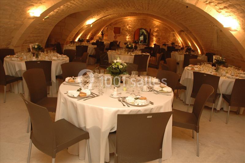 Salle voûtée élégamment décorée avec des tables rondes dressées pour un repas ou un événement.