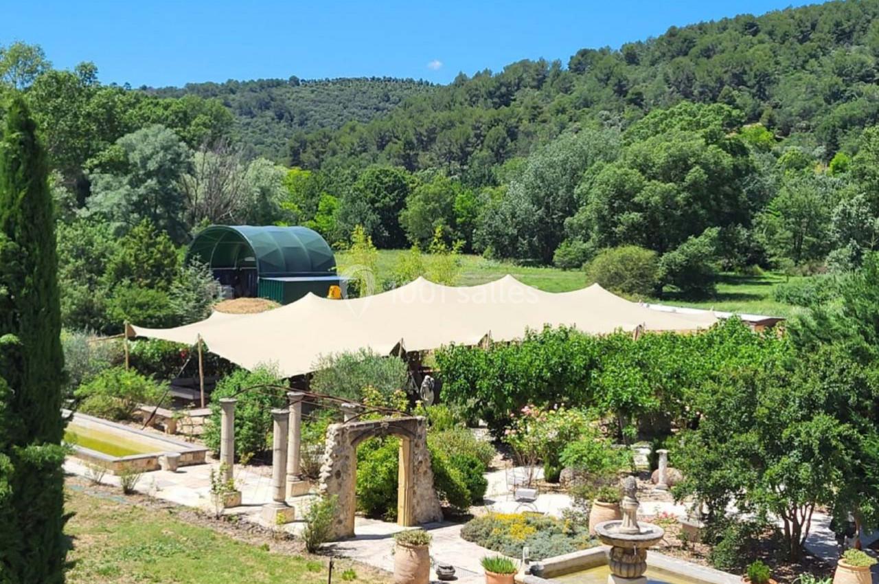 Vue d'un jardin méditerranéen avec une pergola ombragée, entouré de végétation luxuriante et de collines boisées.