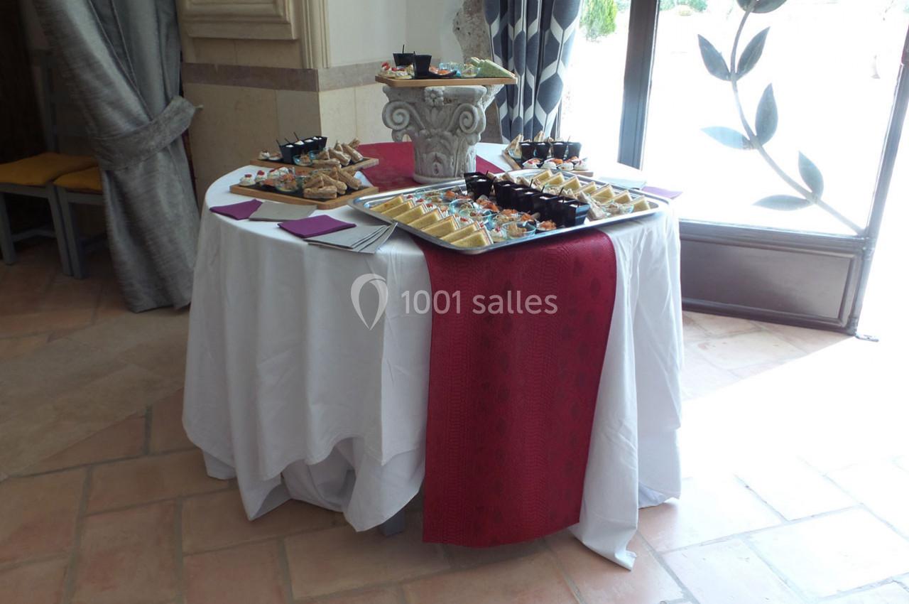 Table ronde dressée avec nappe blanche et chemin de table rouge, garnie de plateaux de bouchées apéritives variées.