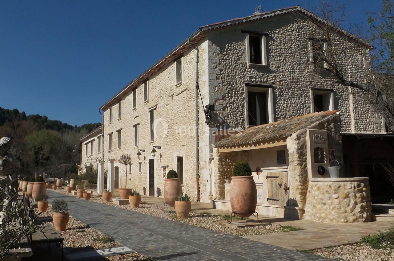 Bâtisse en pierre de style provençal avec chemin pavé, pots en terre cuite et végétation environnante.