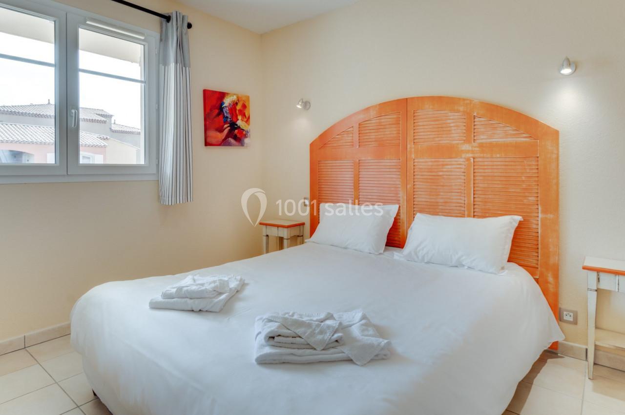 Chambre lumineuse avec un lit double, des tables de chevet, une fenêtre et un tableau coloré au mur.