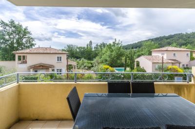 Salon lumineux avec canapé en cuir brun, table basse et accès à un balcon meublé donnant sur un paysage verdoyant.