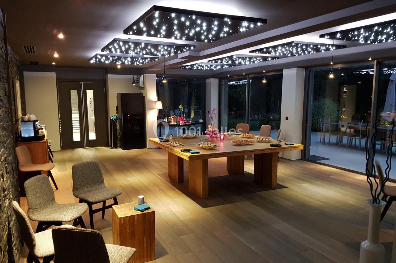 Salle moderne avec éclairage étoilé, table centrale en bois garnie de collations, chaises et grandes baies vitrées donnant…