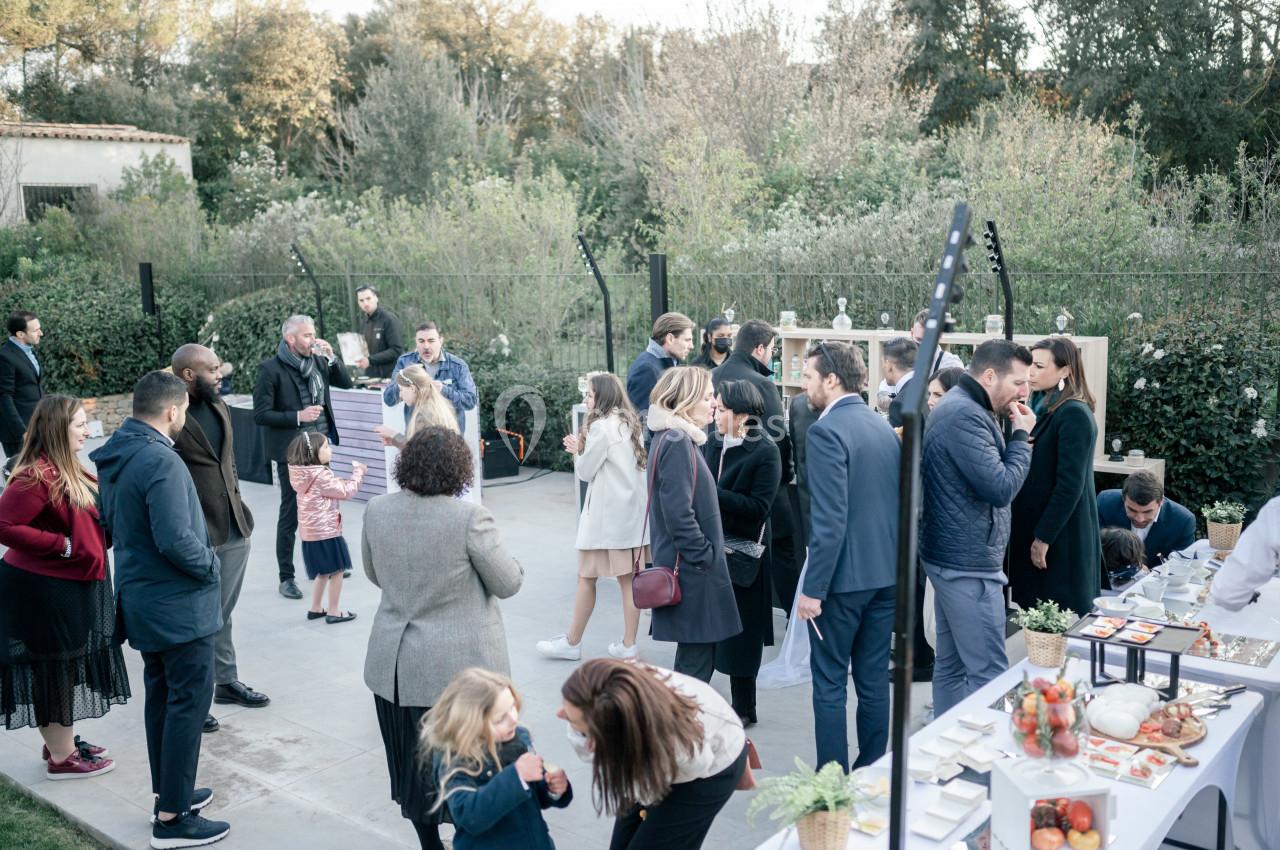 Groupe de personnes rassemblées en extérieur lors d'un événement, discutant près de tables avec des plats et boissons.