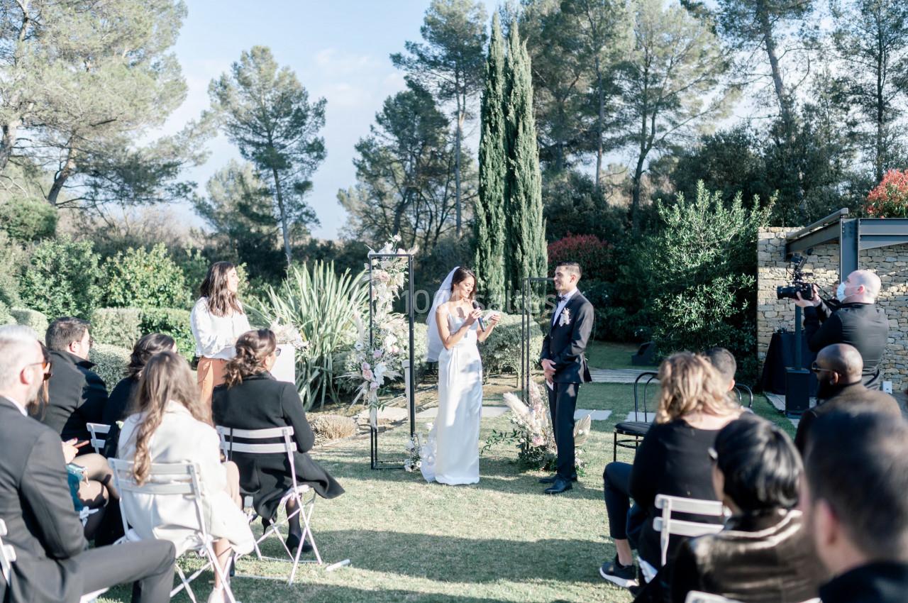 Un couple échange ses vœux lors d'une cérémonie de mariage en plein air, entouré d'invités assis.
