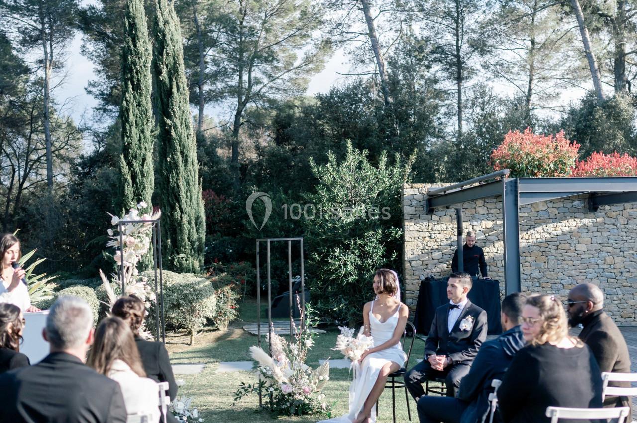 Cérémonie de mariage en extérieur avec des invités assis, un couple au centre et un décor naturel de verdure.