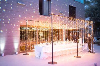 Table dressée pour un dîner en extérieur sous une structure lumineuse avec guirlandes, près d'un bâtiment moderne.