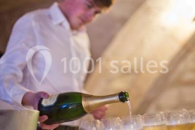 Deux lits simples avec draps rouges dans une chambre lumineuse en pierre, équipée d'une fenêtre et d'un bureau.