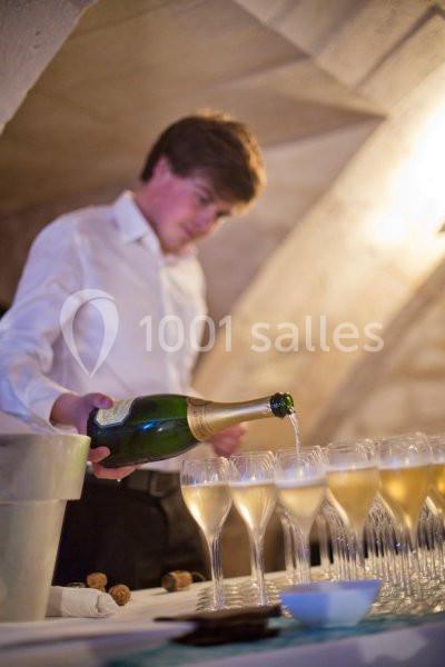 Un serveur verse du champagne dans des flûtes alignées sur une table dans un cadre voûté.