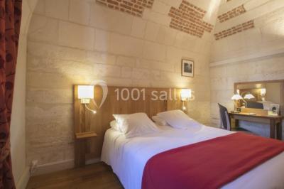 Deux lits simples avec draps rouges dans une chambre lumineuse en pierre, équipée d'une fenêtre et d'un bureau.