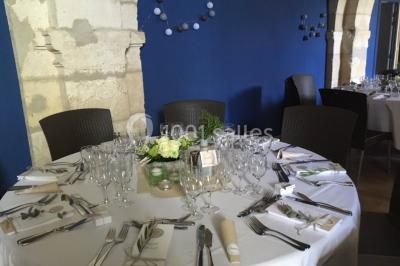 Deux lits simples avec draps rouges dans une chambre lumineuse en pierre, équipée d'une fenêtre et d'un bureau.