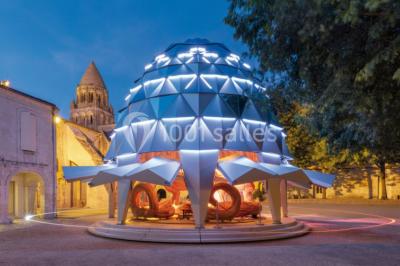 Deux lits simples avec draps rouges dans une chambre lumineuse en pierre, équipée d'une fenêtre et d'un bureau.