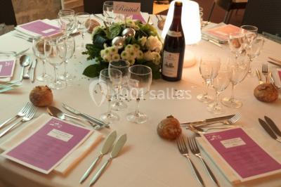 Deux lits simples avec draps rouges dans une chambre lumineuse en pierre, équipée d'une fenêtre et d'un bureau.