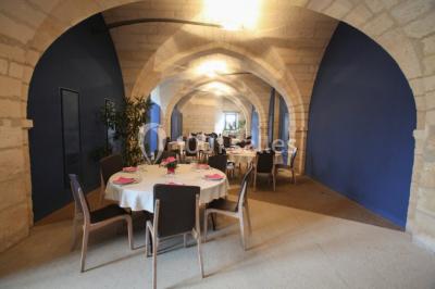 Deux lits simples avec draps rouges dans une chambre lumineuse en pierre, équipée d'une fenêtre et d'un bureau.