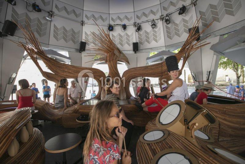 Des personnes interagissent avec des installations en bois et des tambours dans un espace moderne et lumineux.