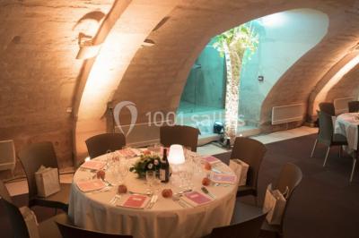 Deux lits simples avec draps rouges dans une chambre lumineuse en pierre, équipée d'une fenêtre et d'un bureau.