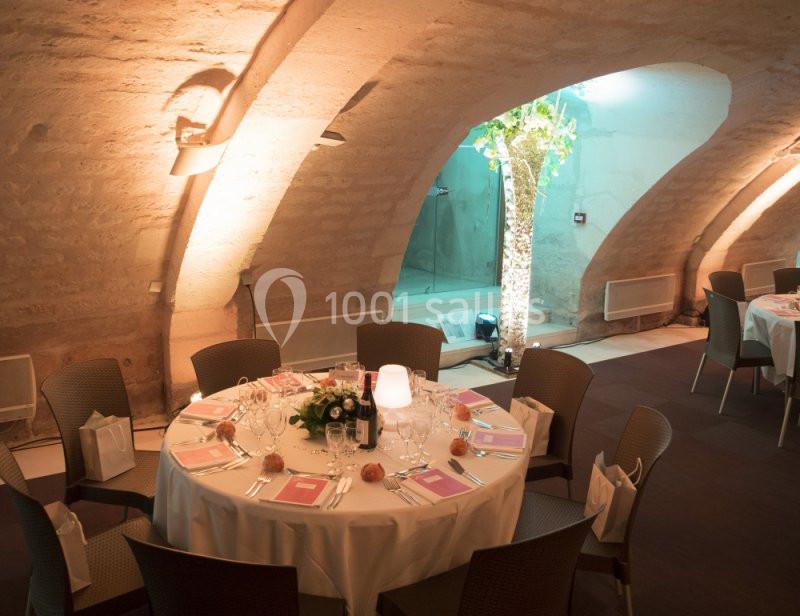 Salle voûtée avec tables rondes dressées pour un repas, éclairage chaleureux et décoration sobre.