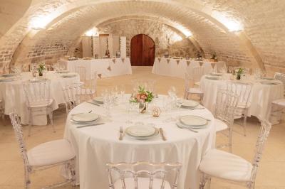 Deux lits simples avec draps rouges dans une chambre lumineuse en pierre, équipée d'une fenêtre et d'un bureau.