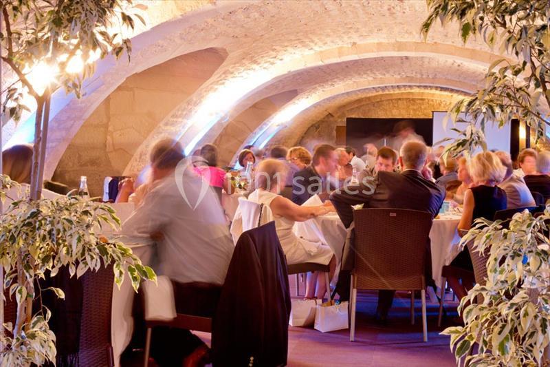 Des convives assis à des tables dans une salle voûtée éclairée, entourée de plantes décoratives.