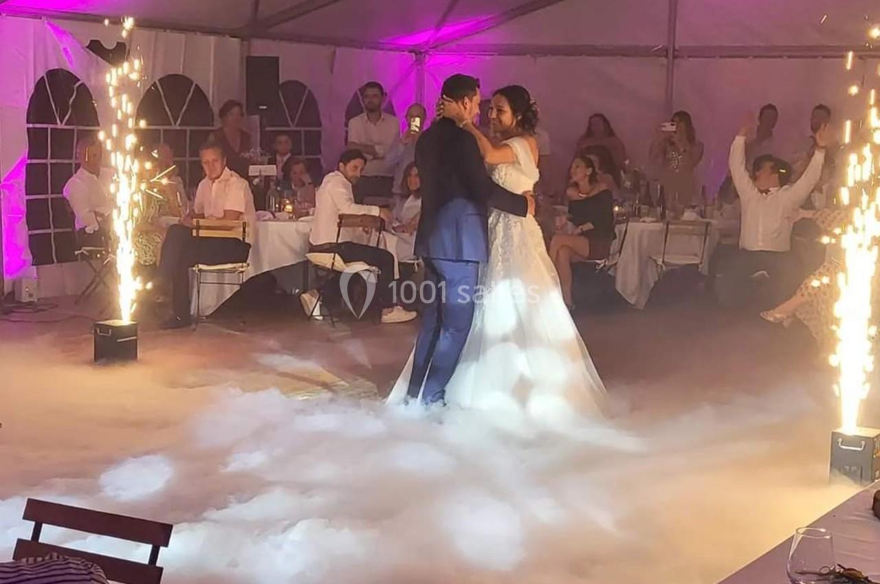 Un couple danse leur première danse de mariage entouré de fumée et de jets d'étincelles dans une salle décorée.