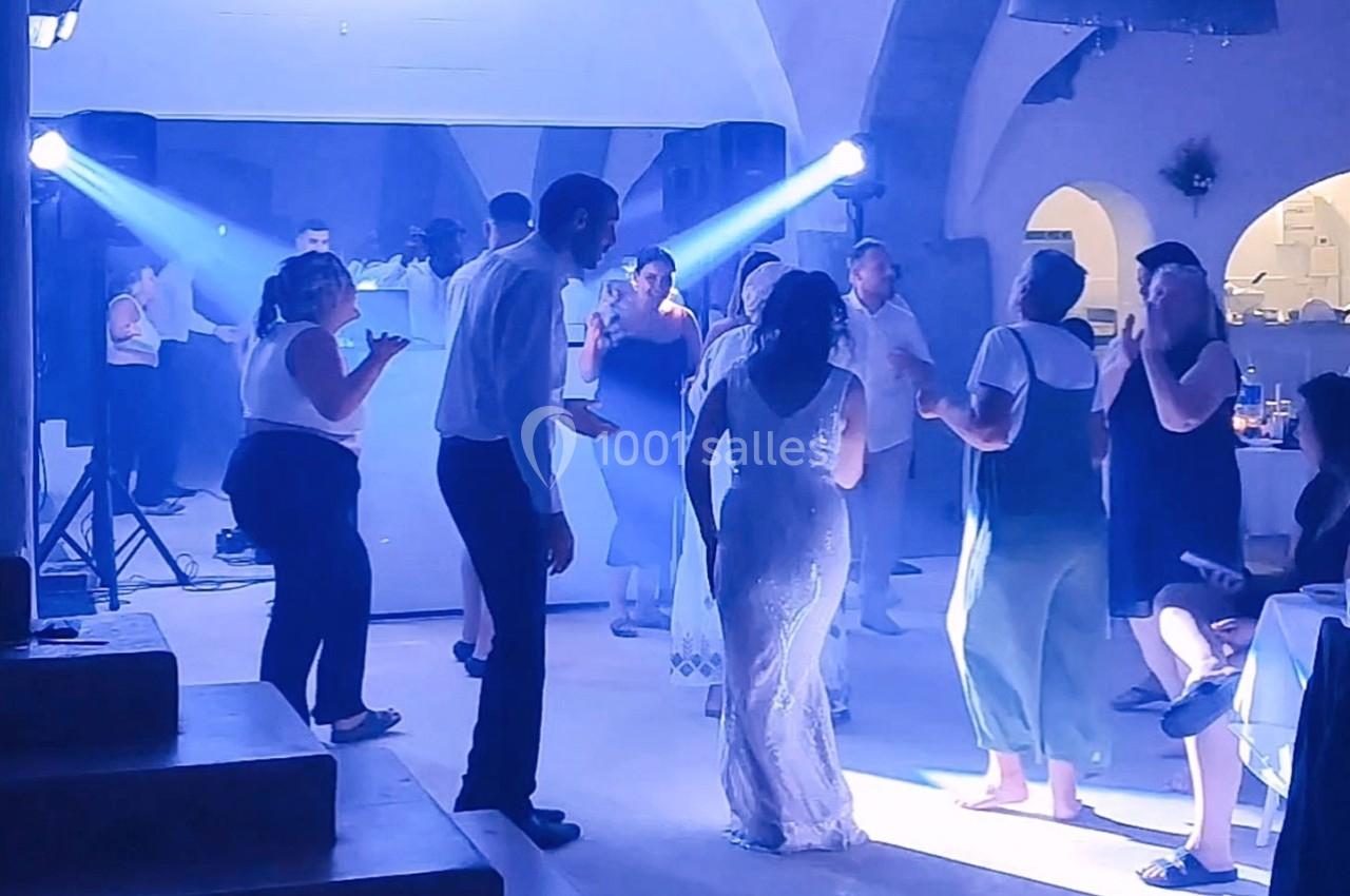 Des personnes dansent dans une salle éclairée par des projecteurs, ambiance festive avec des invités en arrière-plan.