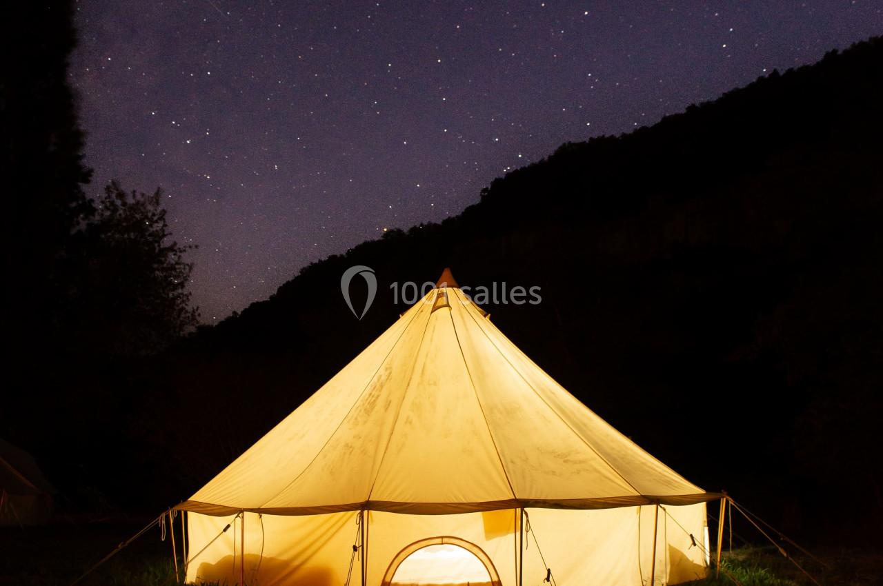 Tente éclairée sous un ciel étoilé dans un paysage nocturne calme.