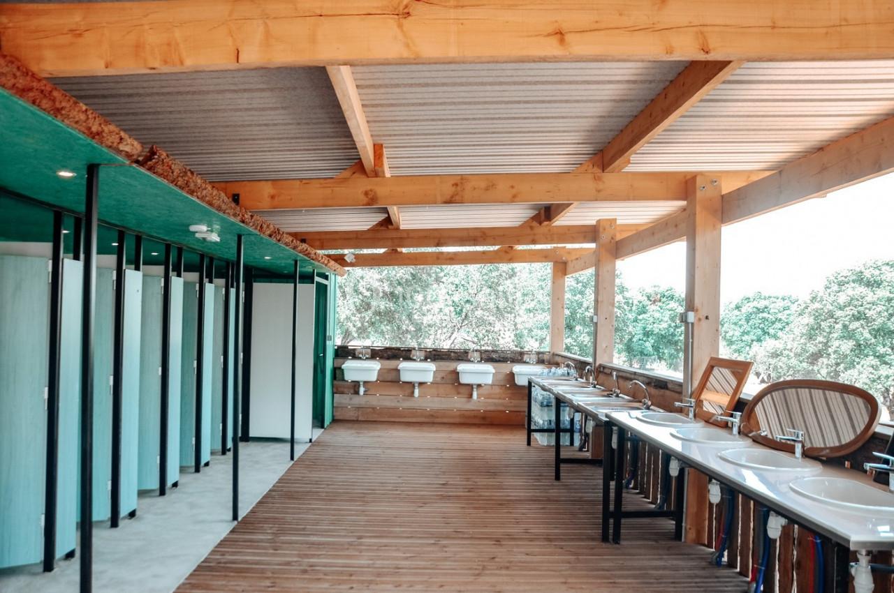 Sanitaires modernes en bois avec cabines, lavabos et vue sur un espace extérieur arboré.
