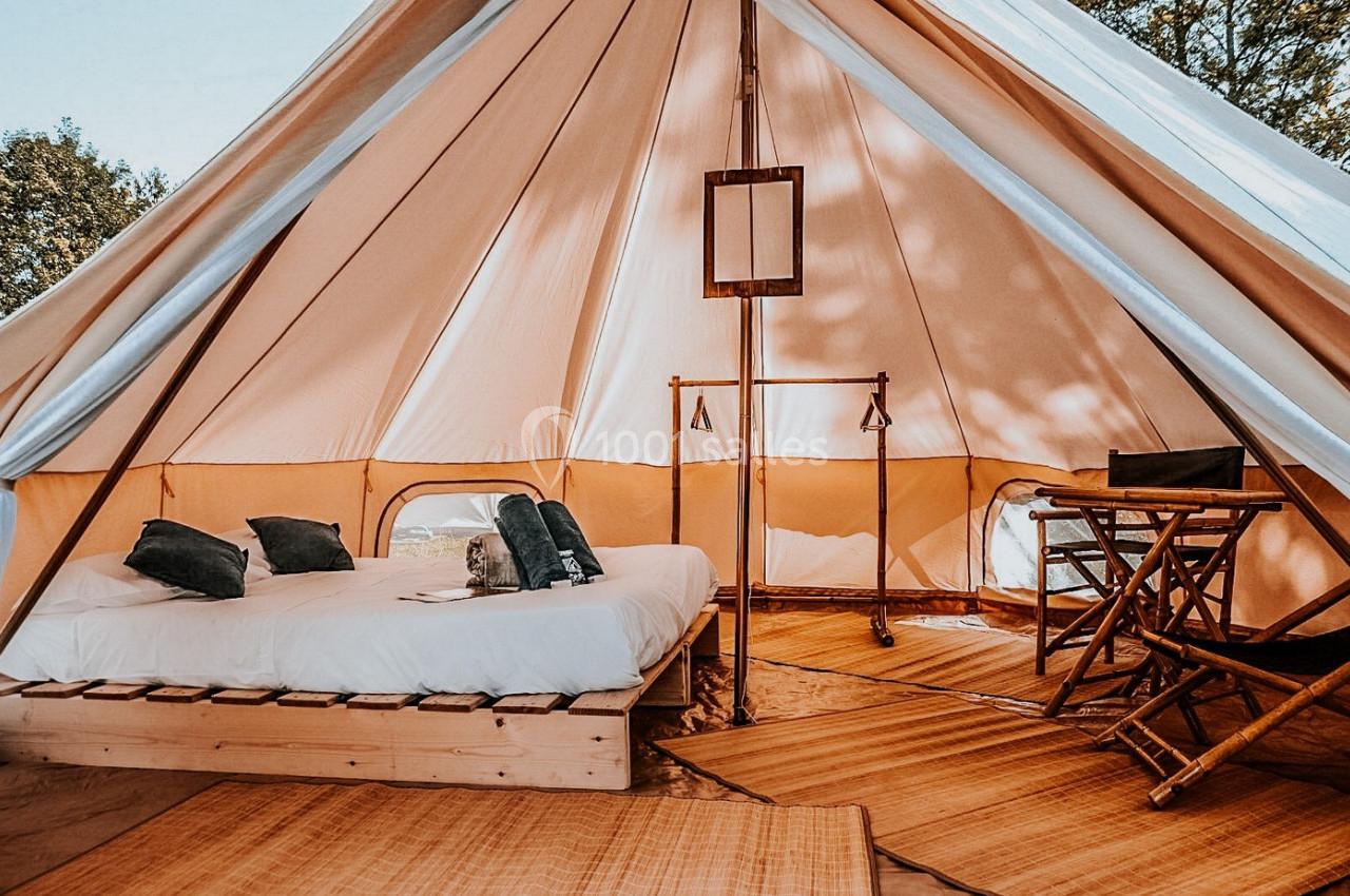 Intérieur d'une tente spacieuse avec lit double, mobilier en bois et lumière naturelle filtrée.