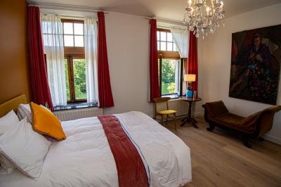 Chambre lumineuse avec lit double, plaid coloré, bureau en bois, chaise et vue sur un jardin par une fenêtre ouverte.