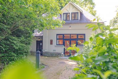 Chambre lumineuse avec lit double, plaid coloré, bureau en bois, chaise et vue sur un jardin par une fenêtre ouverte.