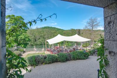 Chambre lumineuse avec lit double, plaid coloré, bureau en bois, chaise et vue sur un jardin par une fenêtre ouverte.