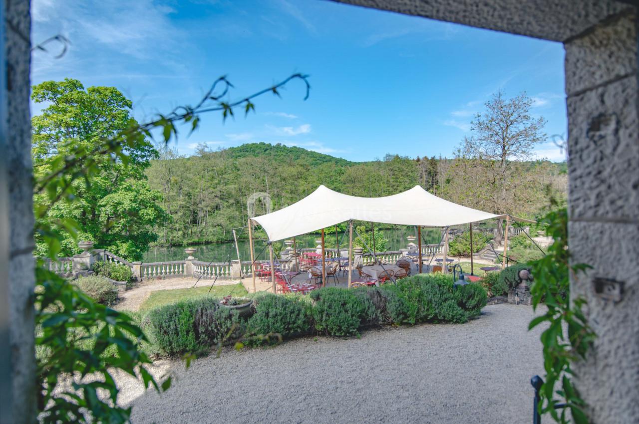 Vue sur une terrasse extérieure ombragée par une toile blanche, entourée de verdure et d'un paysage naturel.