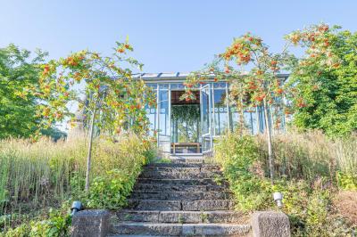 Chambre lumineuse avec lit double, plaid coloré, bureau en bois, chaise et vue sur un jardin par une fenêtre ouverte.