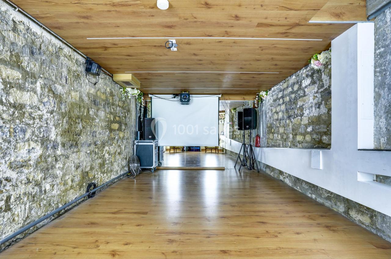 Salle avec murs en pierre, parquet au sol, écran de projection et équipements audio.