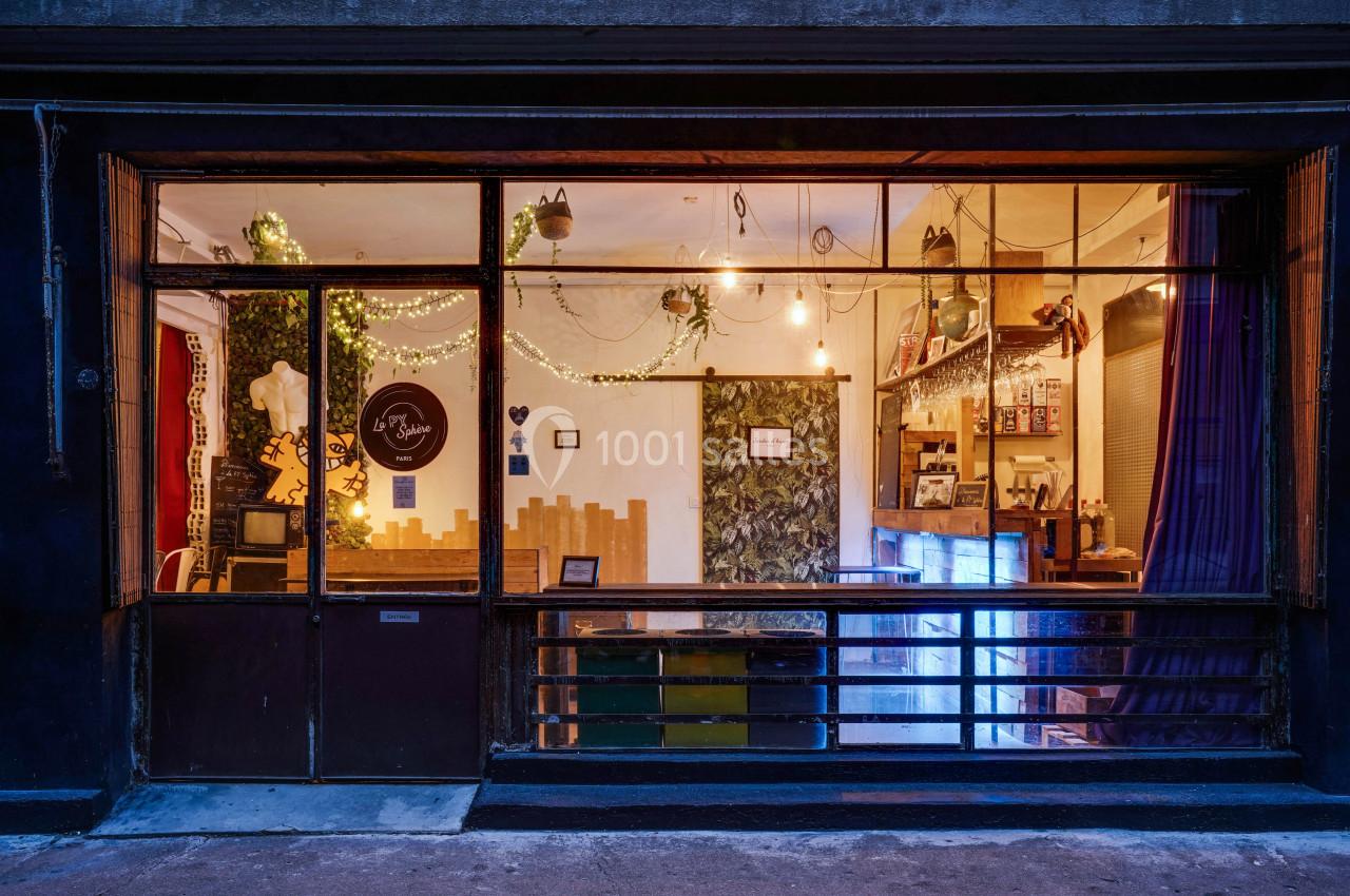 Façade d'une boutique éclairée avec une vitrine décorée de guirlandes lumineuses et un intérieur chaleureux.