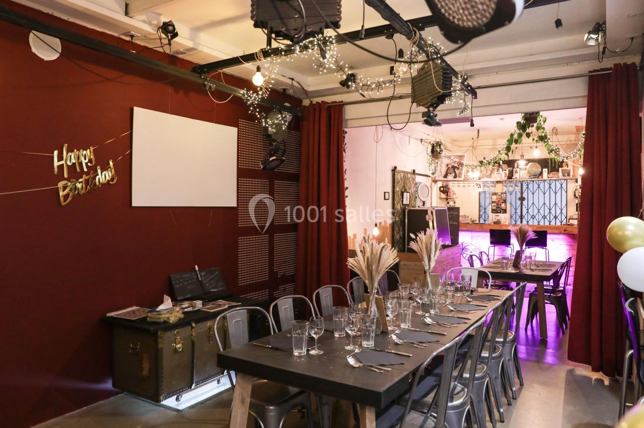 Salle décorée pour un anniversaire avec guirlandes lumineuses, tables dressées et rideaux rouges en arrière-plan.