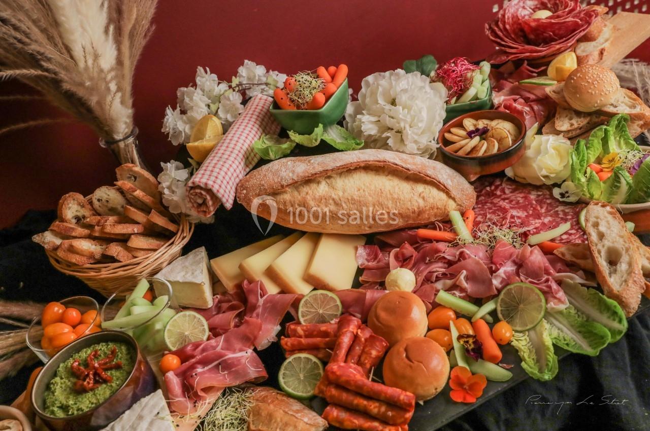Plateau de charcuterie et fromages avec pain, légumes, fruits et sauces, disposés sur une table décorée.