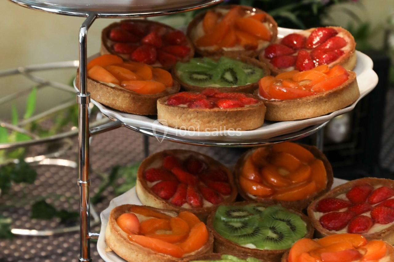 Plateaux de tartes aux fruits variés, garnies de kiwis, fraises et abricots, présentées sur un présentoir à étages.