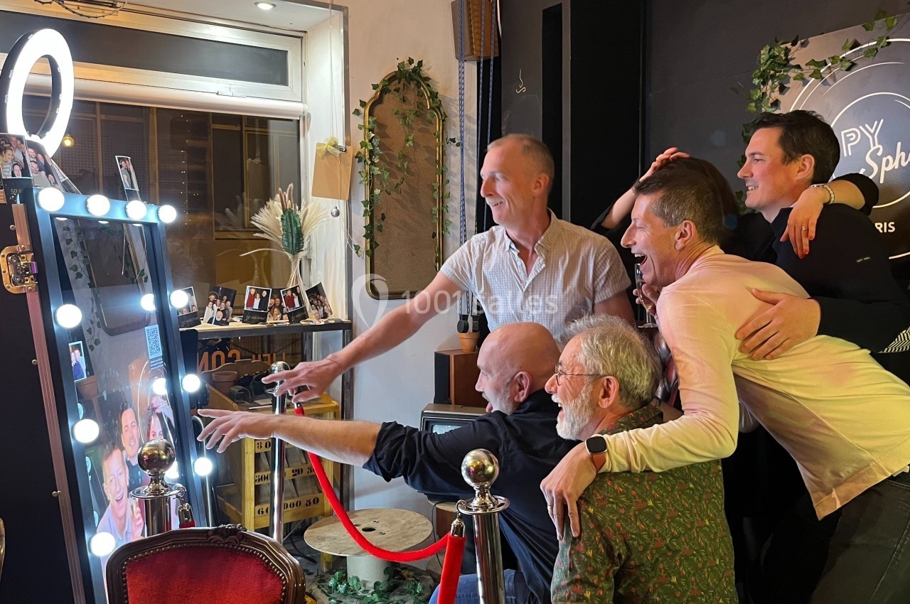Un groupe de personnes souriantes pose devant un photobooth lumineux dans un cadre convivial et décoré.