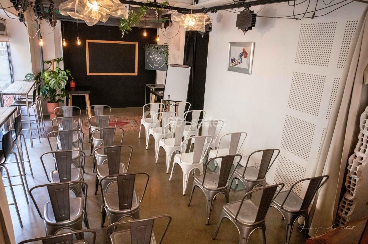 Salle de réunion lumineuse avec des chaises en métal disposées face à un tableau noir et un chevalet.