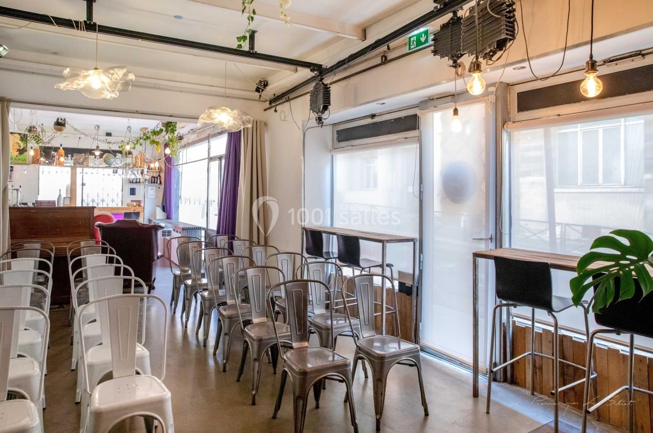 Salle lumineuse avec chaises métalliques alignées, comptoir en bois au fond et grandes fenêtres laissant entrer la lumière.