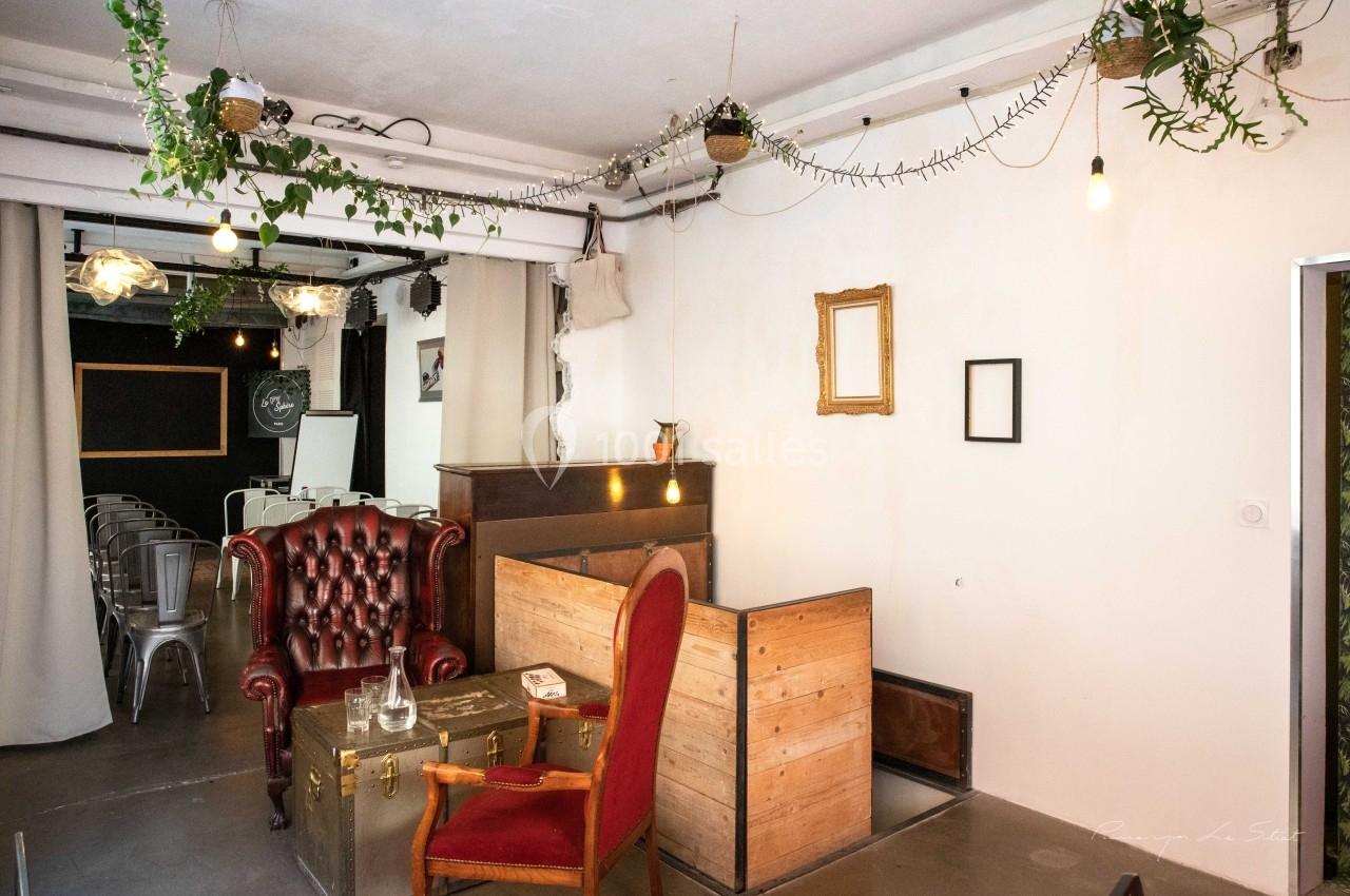 Espace intérieur avec fauteuils vintage, plantes suspendues, éclairage tamisé et mobilier en bois.