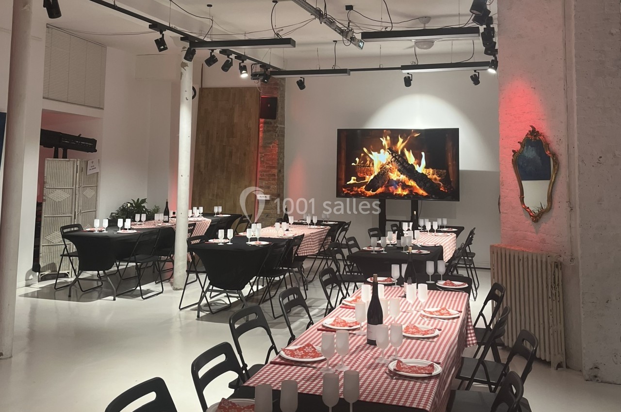 Salle aménagée pour un repas, avec tables dressées, nappes à carreaux rouges et écran affichant une cheminée.